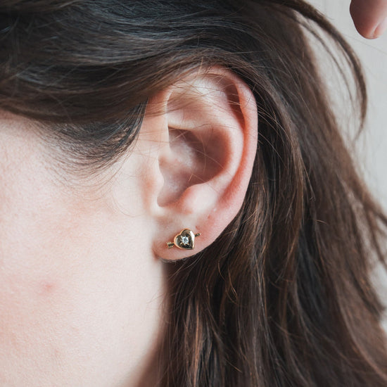 Dainty gold heart stud earrings with arrow details and sparkling center moissanite stones