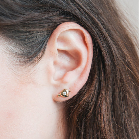 Dainty gold heart stud earrings with arrow details and sparkling center moissanite stones