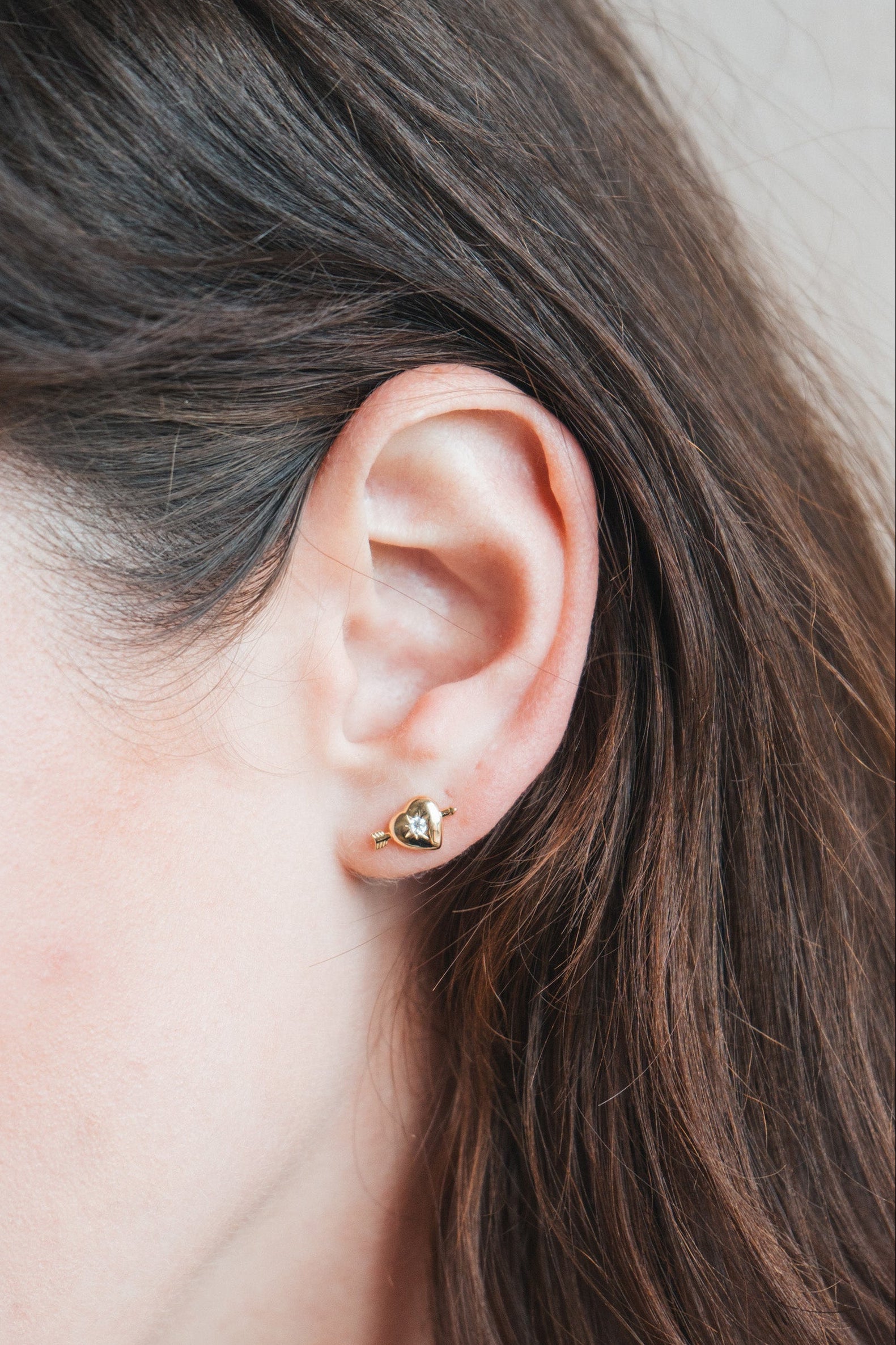 Dainty gold heart stud earrings with arrow details and sparkling center moissanite stones