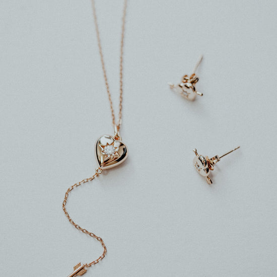 Dainty gold heart stud earrings with arrow details and sparkling center moissanite stones