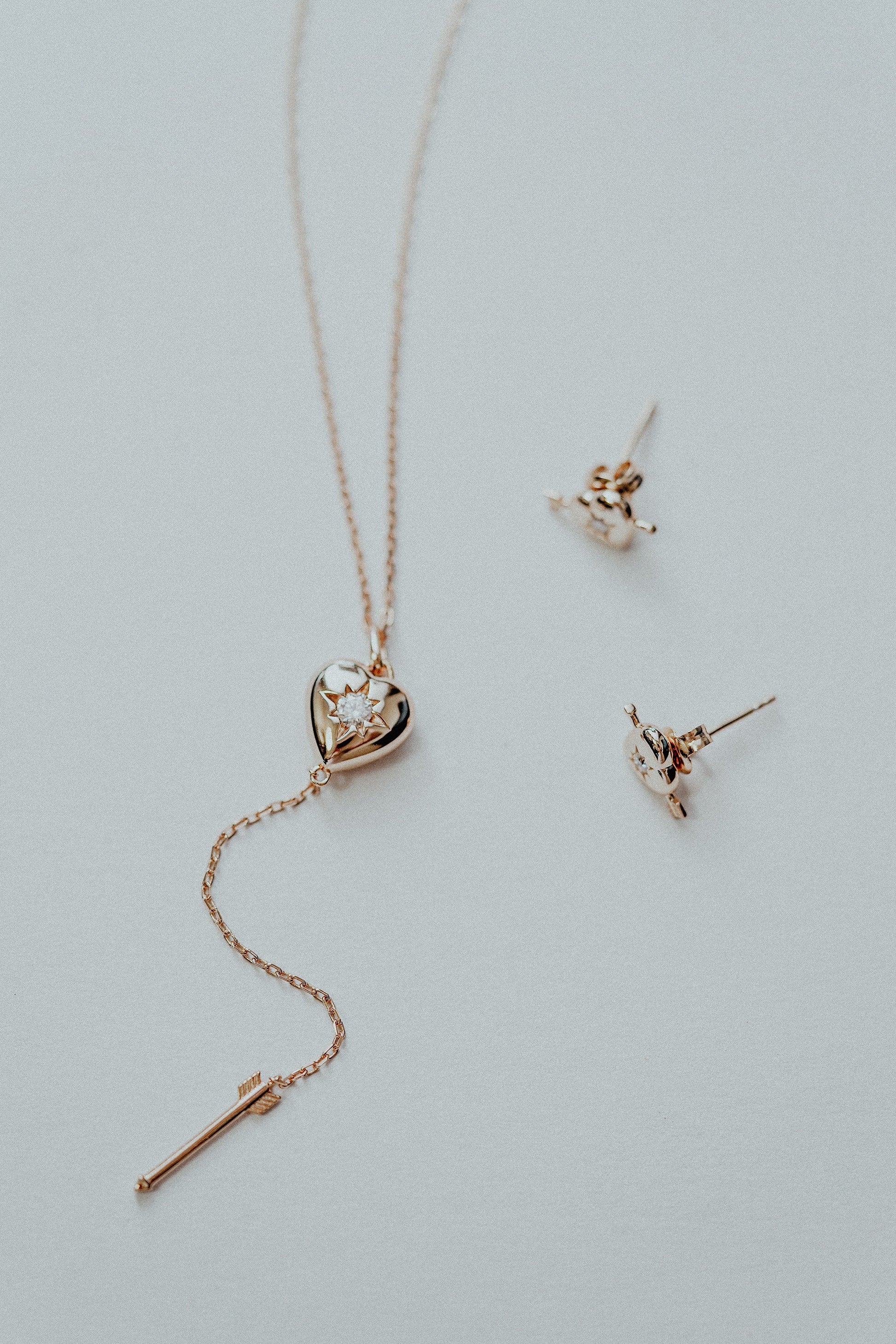 Dainty gold heart stud earrings with arrow details and sparkling center moissanite stones