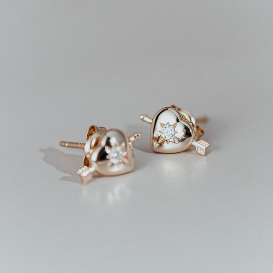 Dainty gold heart stud earrings with arrow details and sparkling center moissanite stones