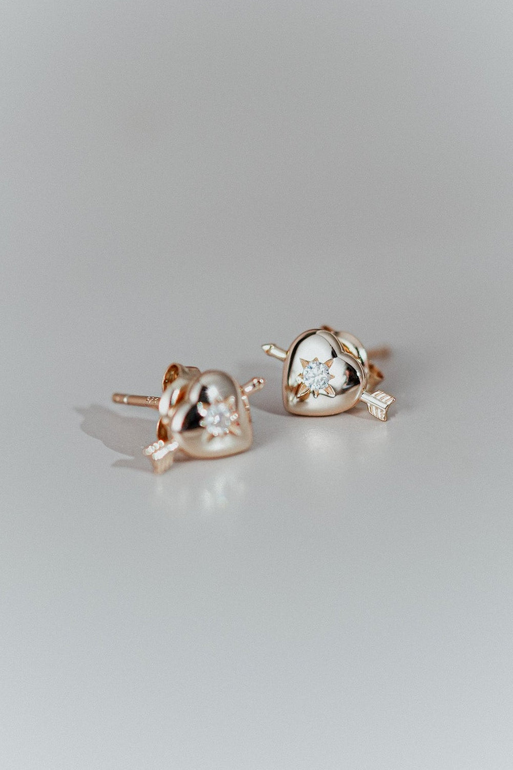 Dainty gold heart stud earrings with arrow details and sparkling center moissanite stones