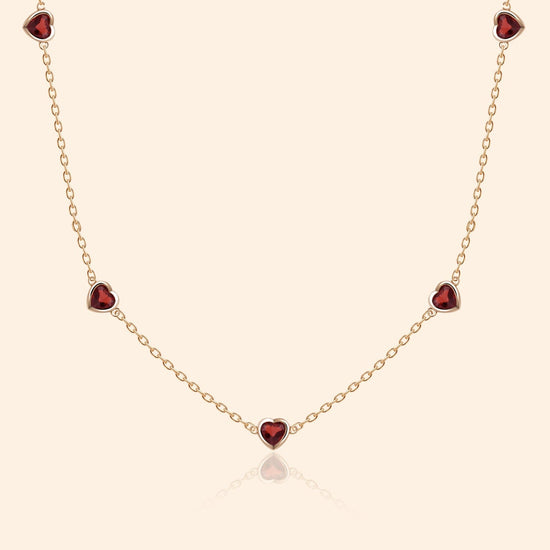 Delicate gold chain necklace featuring five evenly spaced petite red garnet hearts.