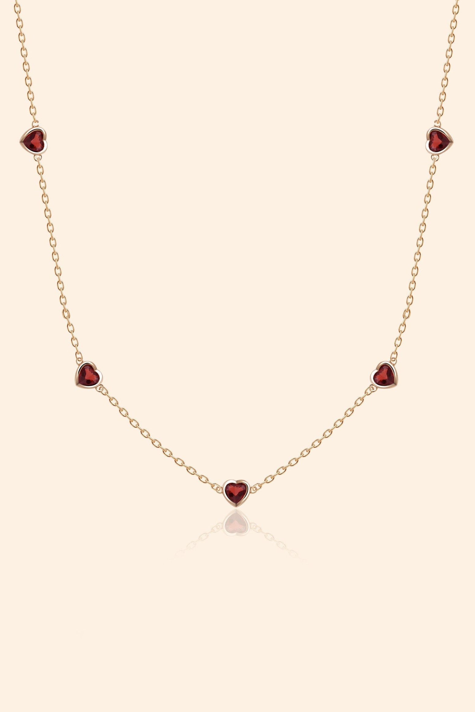 Delicate gold chain necklace featuring five evenly spaced petite red garnet hearts.