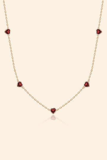 Delicate gold chain necklace featuring five evenly spaced petite red garnet hearts.