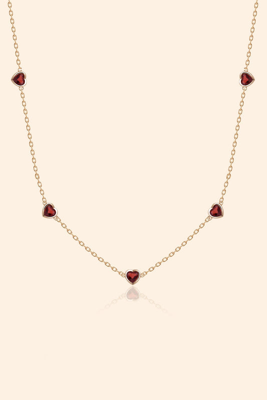 Delicate gold chain necklace featuring five evenly spaced petite red garnet hearts.