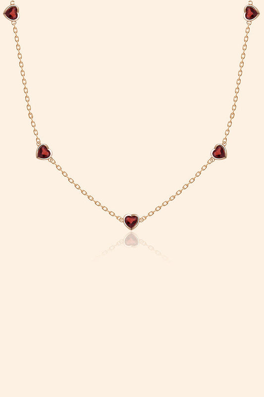 Delicate gold chain necklace featuring five evenly spaced petite red garnet hearts.