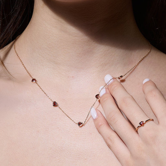 Delicate gold chain necklace featuring five evenly spaced petite red garnet hearts.