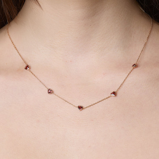 Delicate gold chain necklace featuring five evenly spaced petite red garnet hearts.