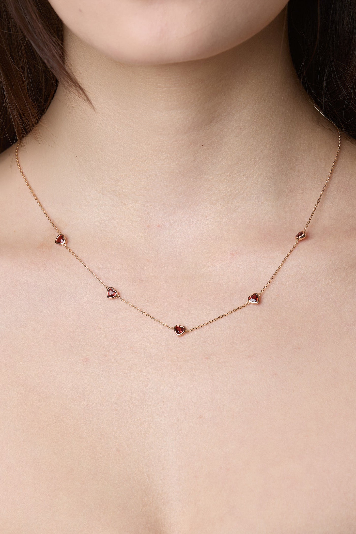 Delicate gold chain necklace featuring five evenly spaced petite red garnet hearts.