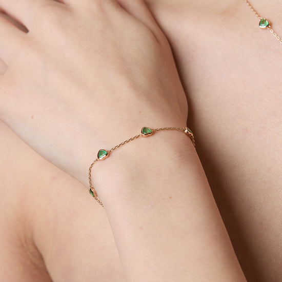 A delicate gold station necklace adorned with four petite, translucent heart-shaped green chalcedony gemstones.