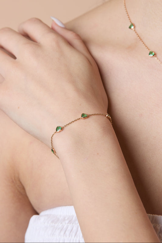 A delicate gold station necklace adorned with four petite, translucent heart-shaped green chalcedony gemstones.