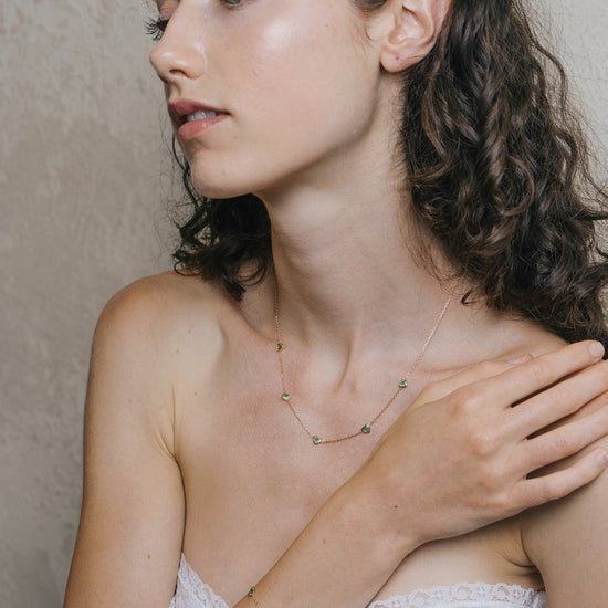 A delicate gold station bracelet adorned with four petite, translucent heart-shaped green chalcedony gemstones.