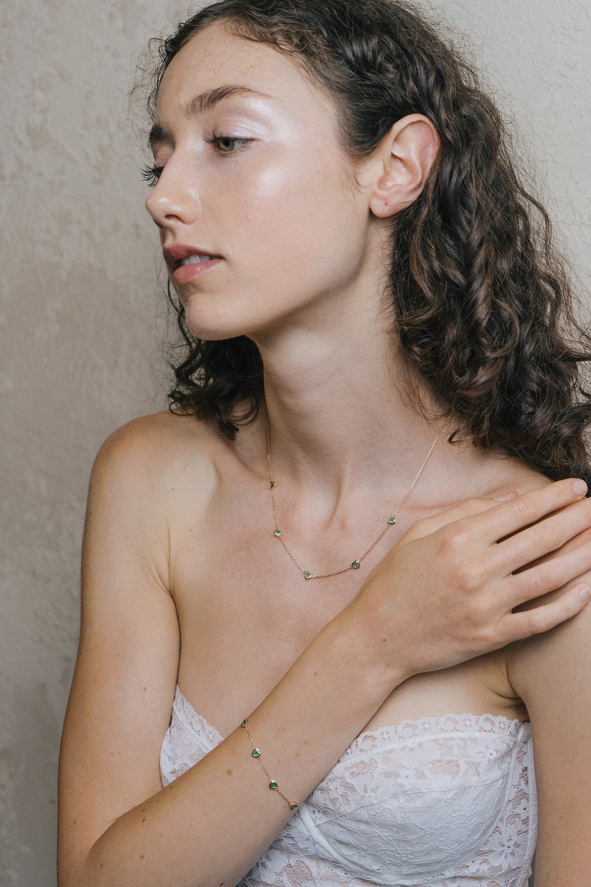 A delicate gold station bracelet adorned with four petite, translucent heart-shaped green chalcedony gemstones.