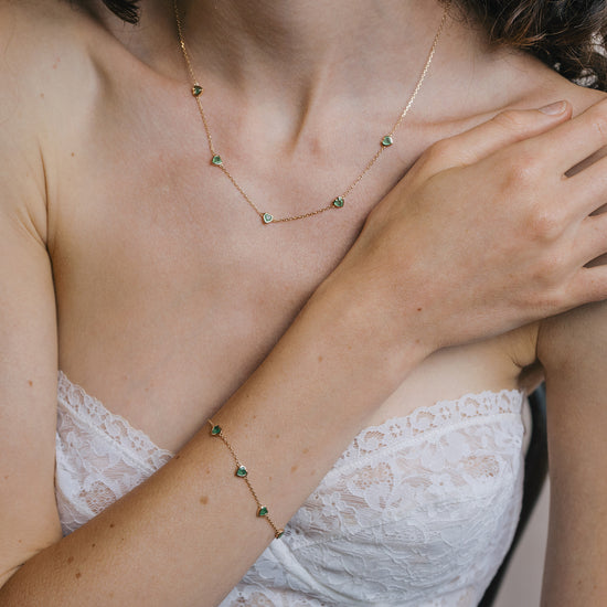 A delicate gold station bracelet adorned with four petite, translucent heart-shaped green chalcedony gemstones.