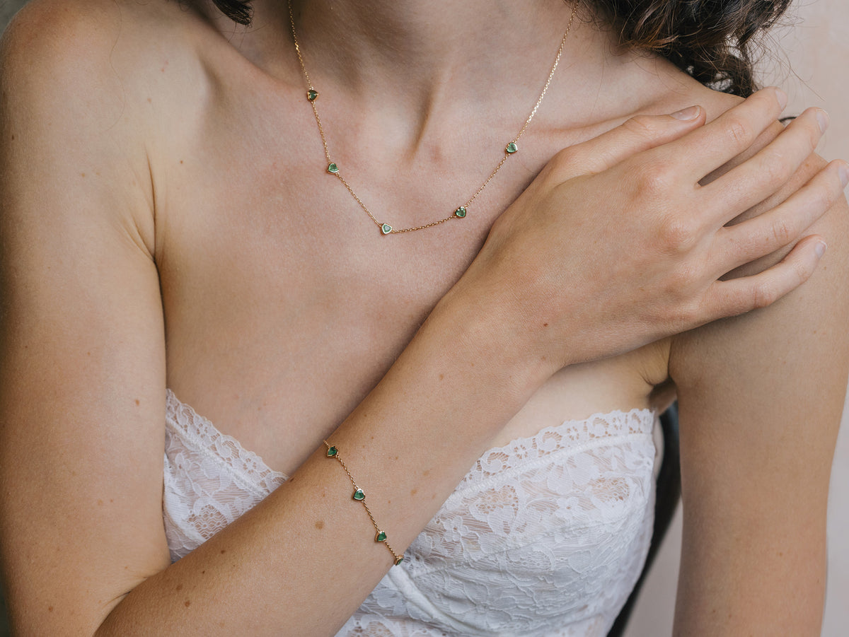 A delicate gold station bracelet adorned with four petite, translucent heart-shaped green chalcedony gemstones.