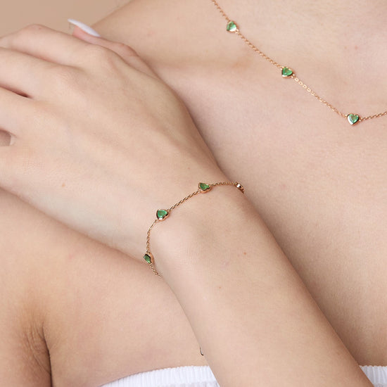 A delicate gold station necklace adorned with four petite, translucent heart-shaped green chalcedony gemstones.