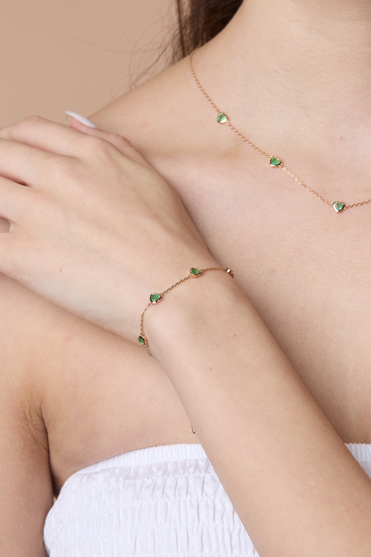A delicate gold station necklace adorned with four petite, translucent heart-shaped green chalcedony gemstones.