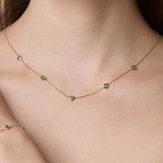 Model wearing a delicate gold station necklace adorned with five petite, translucent heart-shaped green chalcedony gemstones.