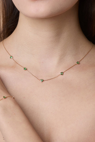 Model wearing a delicate gold station necklace adorned with five petite, translucent heart-shaped green chalcedony gemstones.