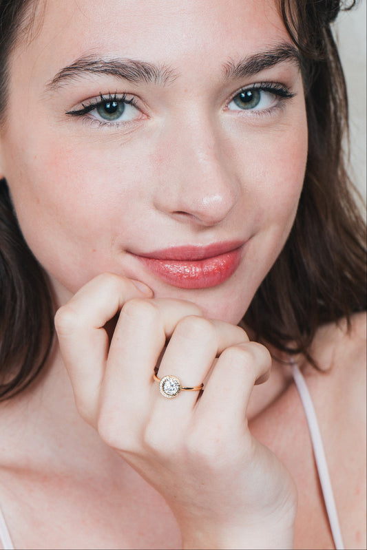 Close-up of a woman wearing a gold halo ring with a diamond on her finger.