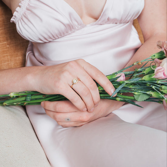 Close-up of a woman wearing a gold halo ring with a diamond on her finger.