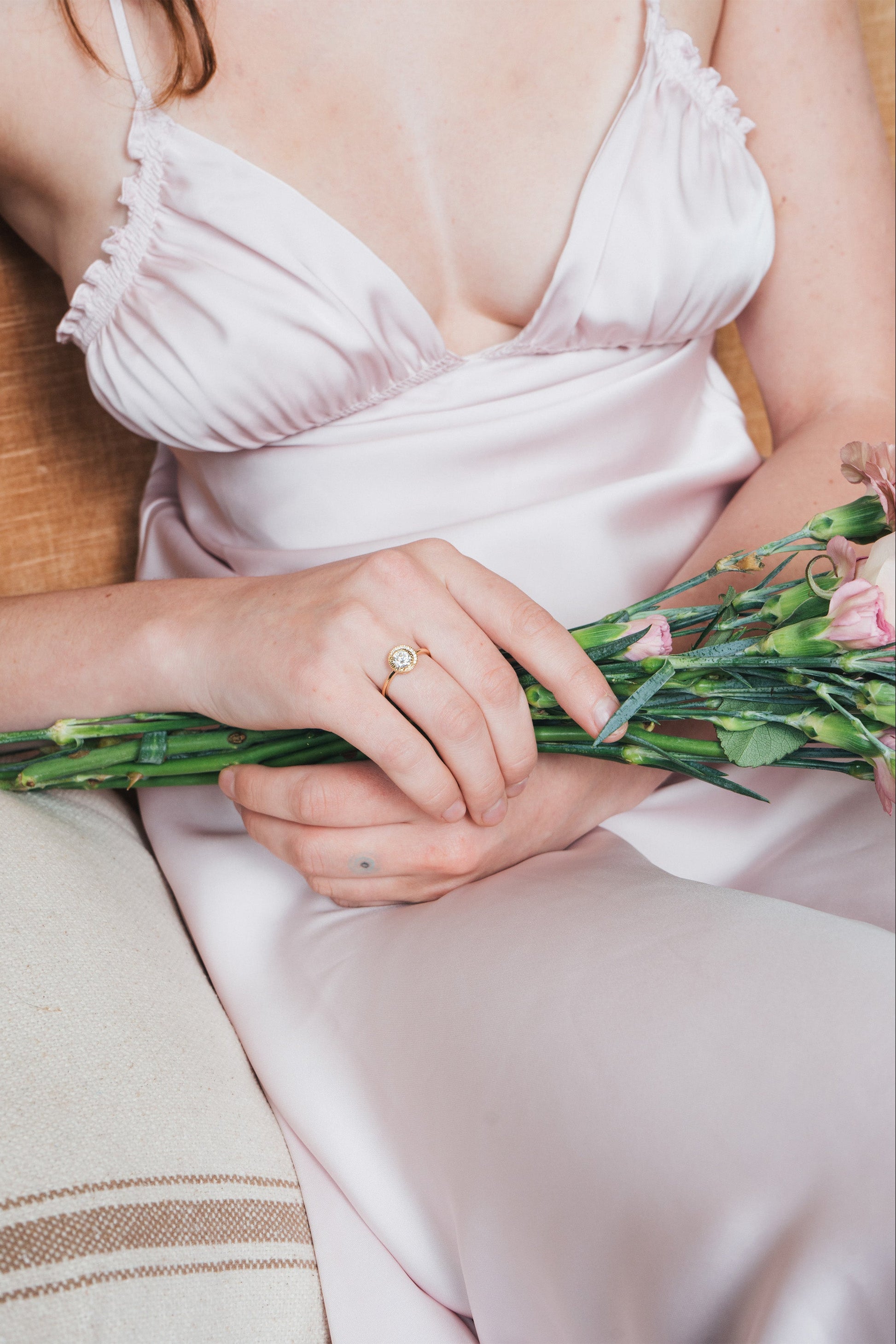 Close-up of a woman wearing a gold halo ring with a diamond on her finger.