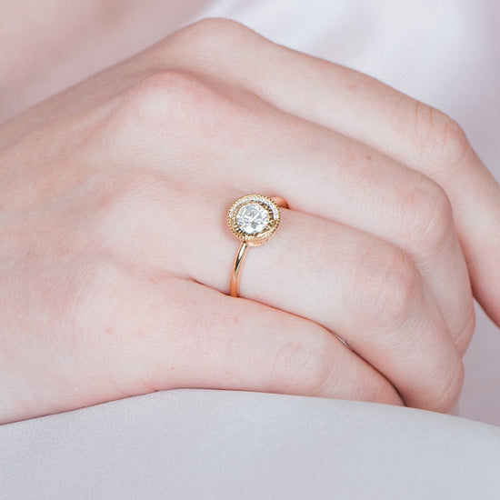Close-up of a woman wearing a gold halo ring with a diamond on her finger.