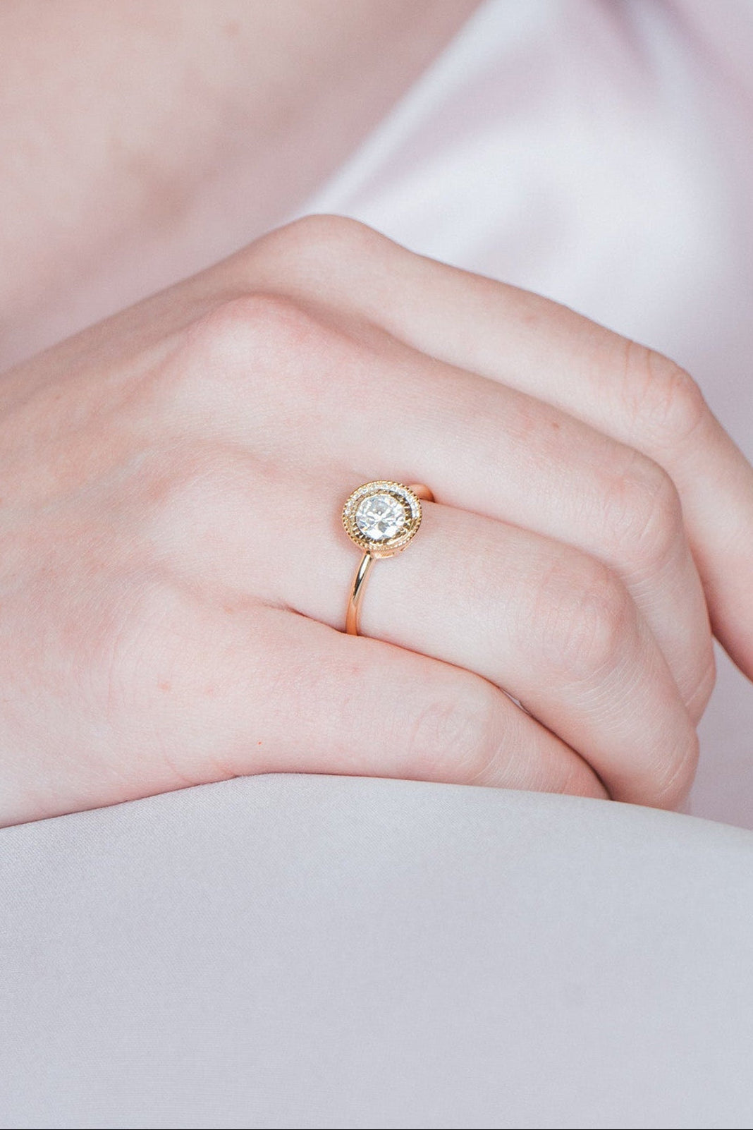 Close-up of a woman wearing a gold halo ring with a diamond on her finger.