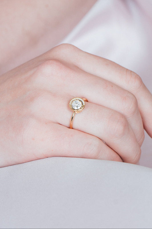 Close-up of a woman wearing a gold halo ring with a diamond on her finger.