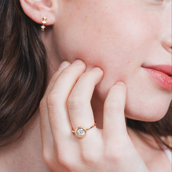 Close-up of a woman wearing a gold halo ring with a diamond on her finger.