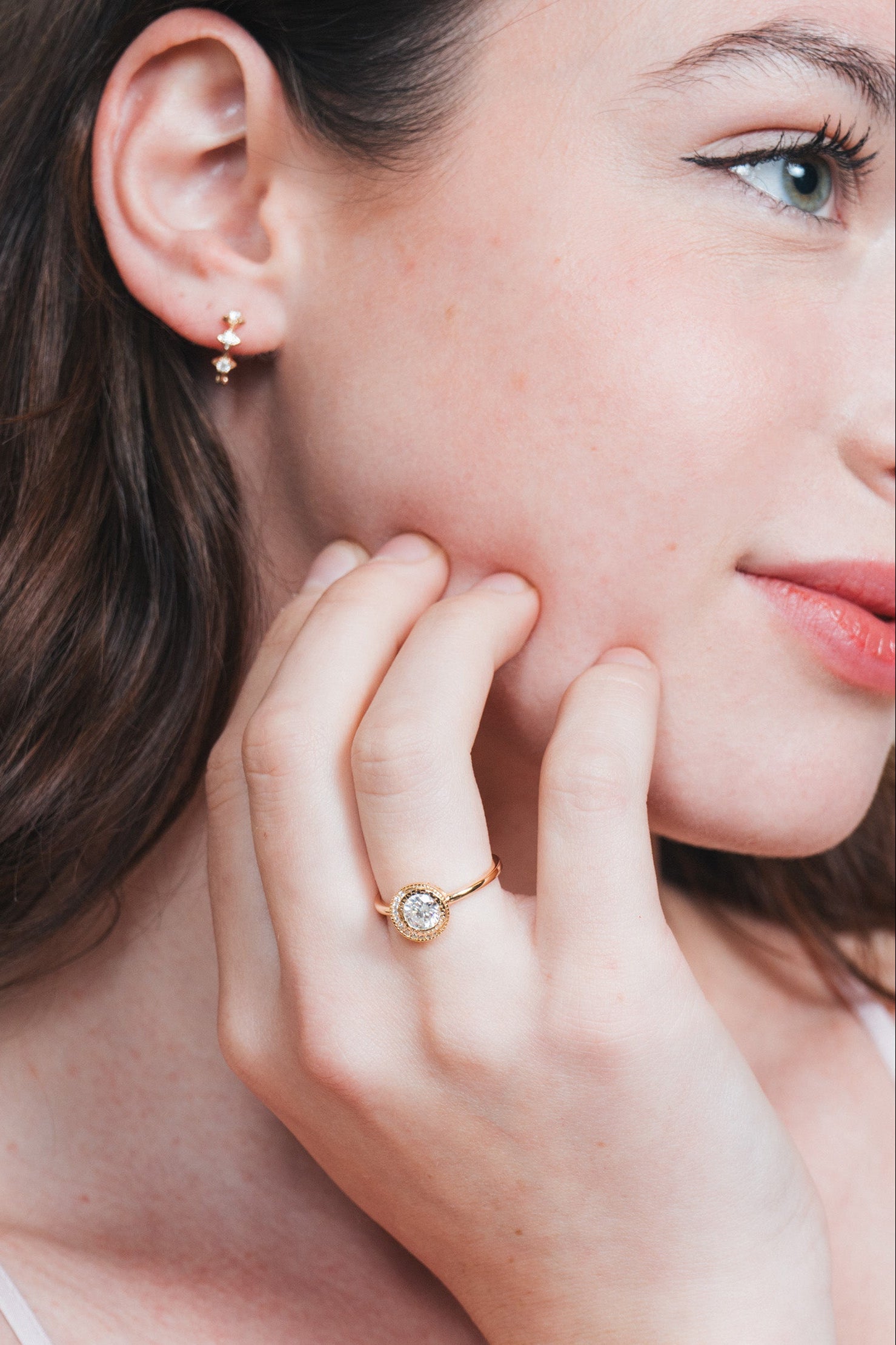 Close-up of a woman wearing a gold halo ring with a diamond on her finger.