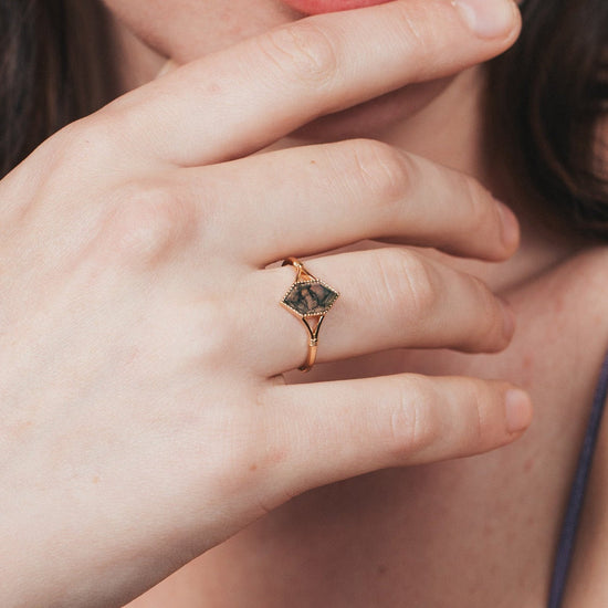 Close-up of a person wearing a gold ring with moss agate.