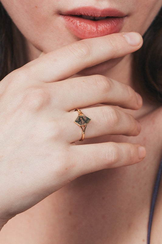 Close-up of a person wearing a gold ring with moss agate.