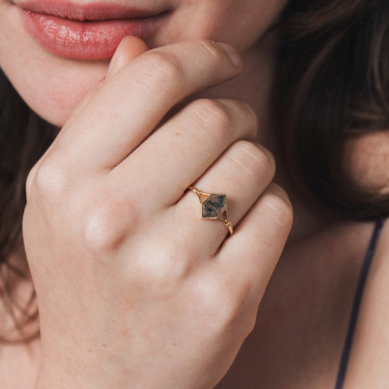 Close-up of a person wearing a gold ring with moss agate.