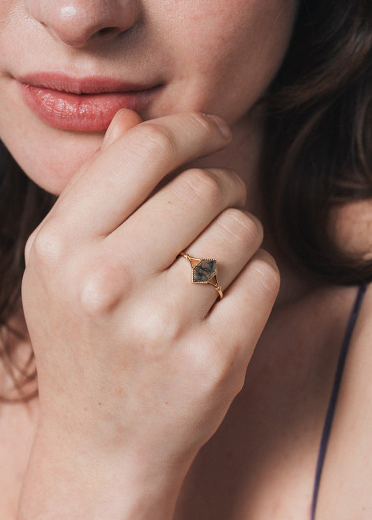 Close-up of a person wearing a gold ring with moss agate.