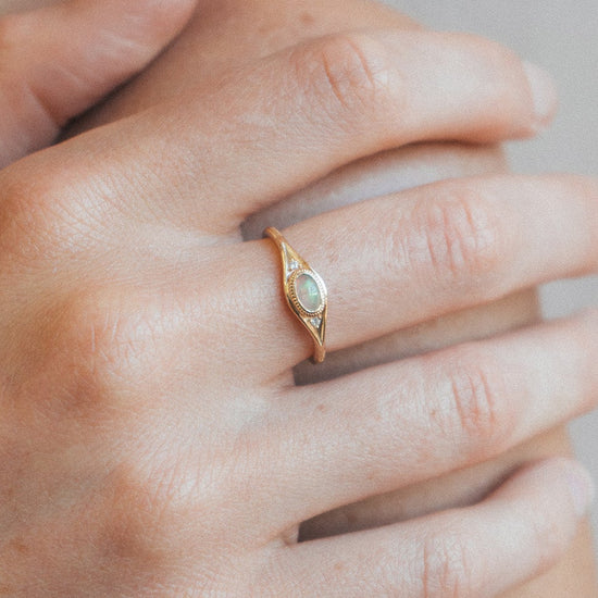 Gold oval opal ring with moissanite accents and vintage-inspired details.