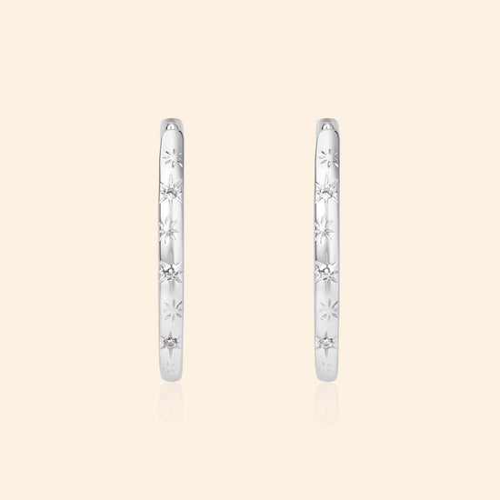 Silver medium hoop earrings with engraved star details and moissanites accents.