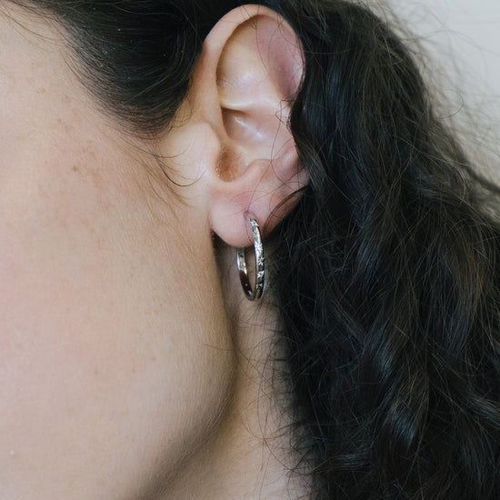 Silver medium hoop earrings with engraved star details and moissanites accents.