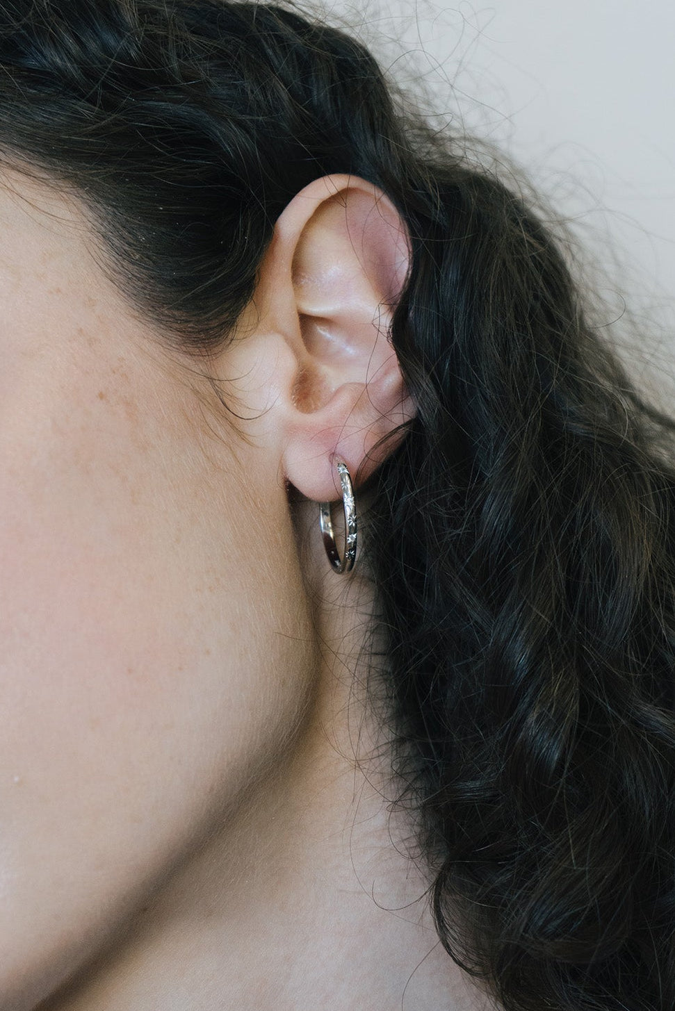 Silver medium hoop earrings with engraved star details and moissanites accents.
