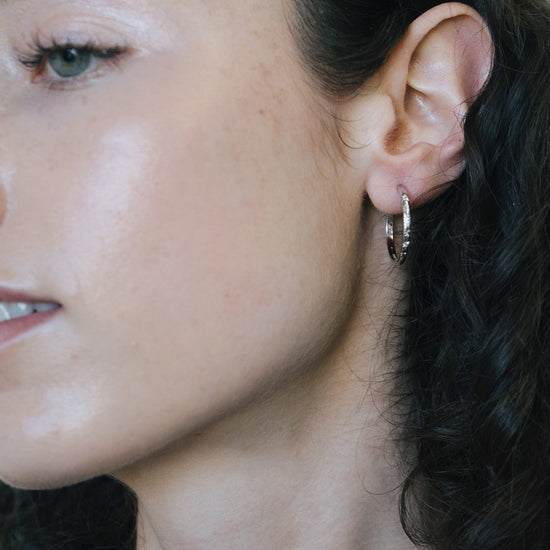 Silver medium hoop earrings with engraved star details and moissanites accents.