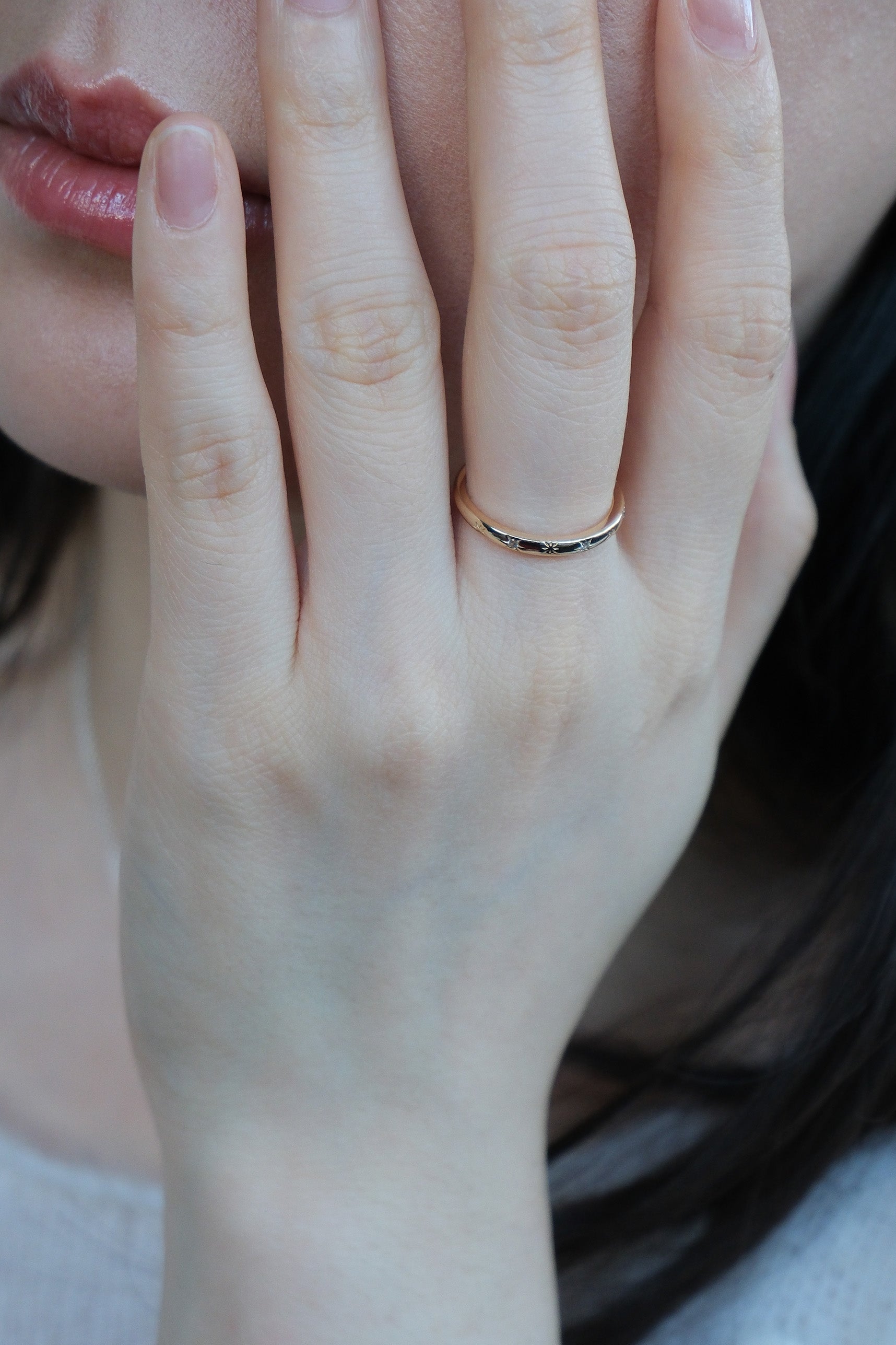Hand wearing a 14K gold plated ring with starburst engravings, celestial jewelry by Lirae.